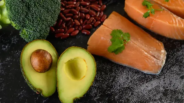 Raw salmon fillets, halved avocado, broccoli and kidney beans on a dark stone bench