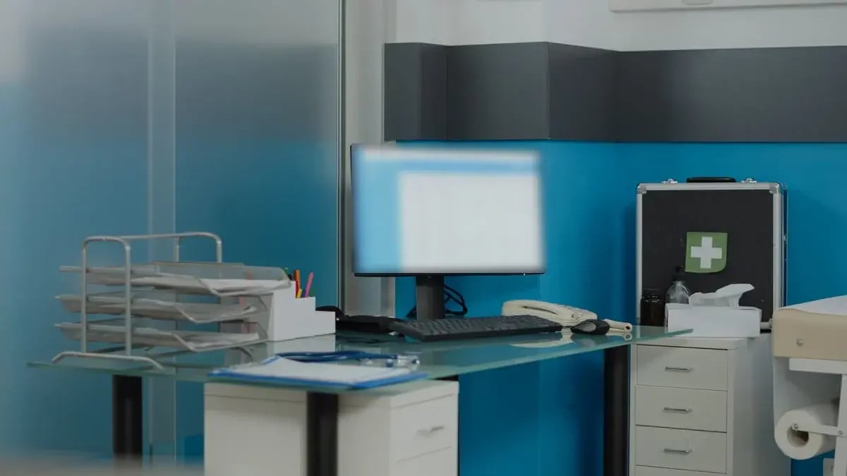 An empty clinic desk with a computer monitor displaying a generic records screen